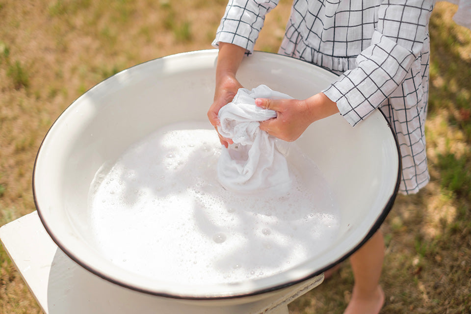 Person washing clothes in a large white basin outdoors.